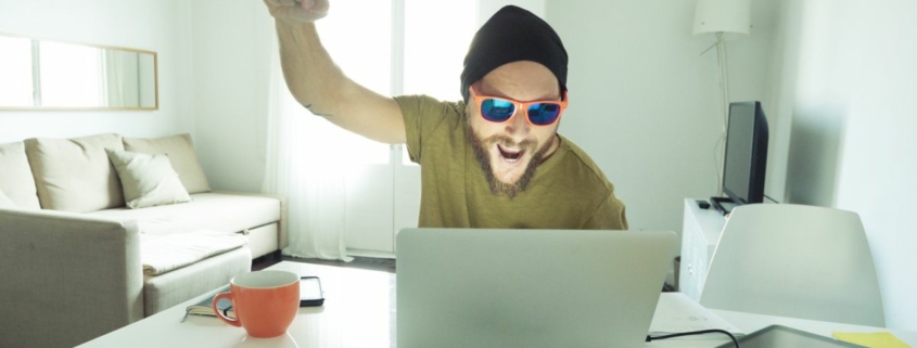 Man celebrates while looking at laptop.