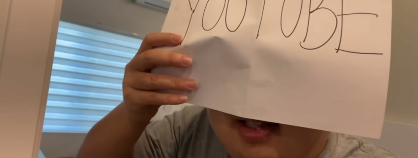 An image of SungWon Cho holding a piece of paper in front of his face reading