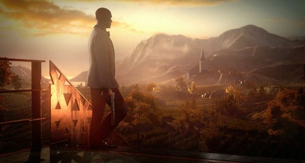 Agent 47 walks in profile, holding a pistol and looking away from the camera towards sunlit mountains in the background.