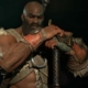 Bearded, Kratos-like Diablo barbarian resting his hands on the pommel of an upturned weapon, looking stoic and wrathful