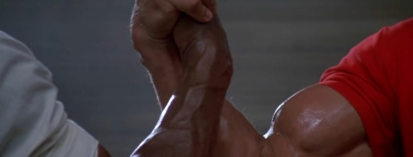 Two glistening, muscular arms shaking hands/arm wrestling in the air sourced from the film Predator