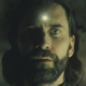 Alan Wake with a glowing bullet hole in his forehead in Alan Wake 2.