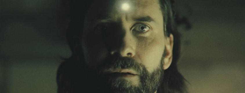 Alan Wake with a glowing bullet hole in his forehead in Alan Wake 2.