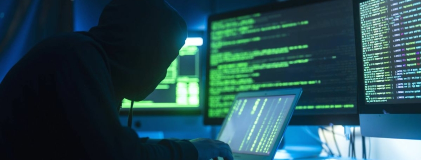 A stylised photograph of a person acting as a hacker, break into servers and infecting them with a virus, as show by computer monitors displaying green text and codes