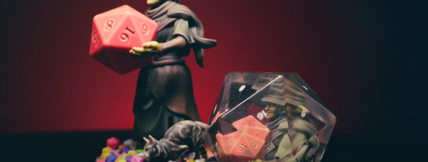 A goblin wizard, holding a dice, and a dice with a goblin wizard holding a dice placed within it.