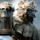 A druid wearing a demonic mask holds up a decaying head in a jar.